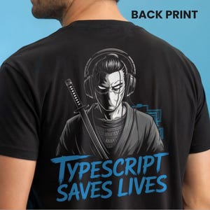 Pode incluir: T-shirt preto com um gráfico de uma figura mascarada com fones de ouvido e uma katana. O design inclui o texto azul "TYPESCRIPT SAVES LIVES". A impressão está na parte de trás da camiseta.