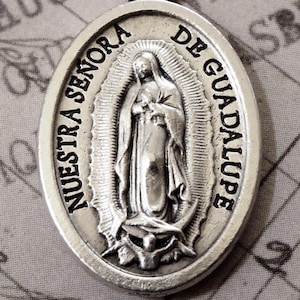 K&ouml;nnte beinhalten: Ovaler Silberanh&auml;nger mit dem Bild Unserer Lieben Frau von Guadalupe, mit dem Text "Nuestra Se&ntilde;ora de Guadalupe". Der Anh&auml;nger hat eine kleine Schlaufe f&uuml;r eine Kette. Der Hintergrund ist ein Vintage-Papier.