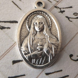May include: Silver oval pendant featuring a religious image of the Virgin Mary with a heart in her hands.