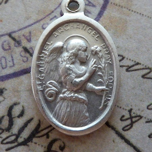 Puede incluir: Pendiente ovalado de plata con una representación del Arcángel Gabriel sosteniendo un lirio. El pendiente tiene la inscripción "St Gabriel Archangel Pray For Us".
