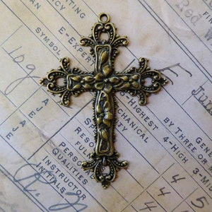 Peut inclure: Un pendentif en forme de croix orné de motifs floraux en bronze. La croix mesure environ 5 cm de haut et possède une boucle en haut pour l'accrocher.