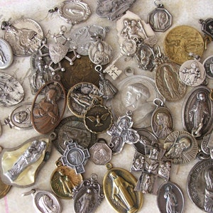 May include: A collection of vintage silver and gold religious medallions with various images of saints and religious symbols. The medallions are in different shapes and sizes and have a worn, antique look.