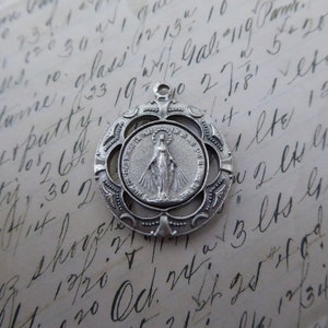 May include: Silver pendant featuring a detailed image of the Virgin Mary with the words "Our Lady of Perpetual Help" and "For Is Who May Ever" surrounding her. The pendant is surrounded by a decorative, openwork frame.