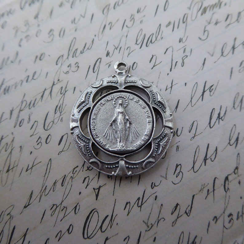 May include: Silver pendant featuring a detailed image of the Virgin Mary with the words "Our Lady of Perpetual Help" and "For Is Who May Ever" surrounding her. The pendant is surrounded by a decorative, openwork frame.