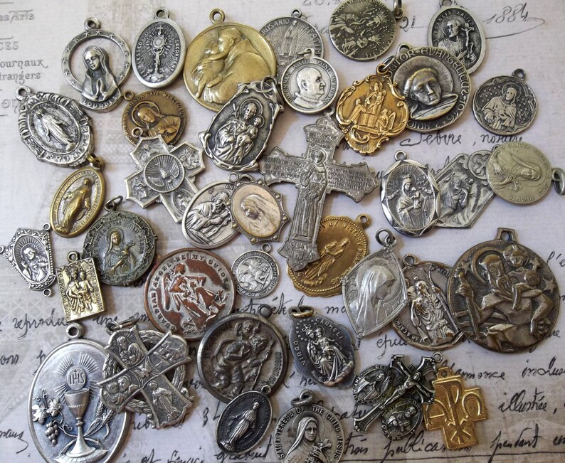 May include: A collection of vintage religious medallions, charms, and pendants. The medallions are made of metal and feature various religious symbols, including crosses, saints, and the Virgin Mary. Some of the medallions are gold-toned, while others are silver-toned.