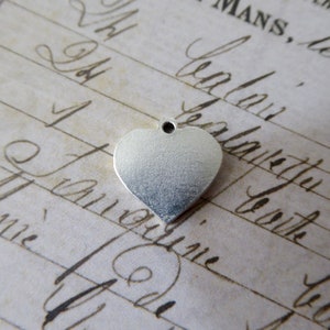 May include: A silver heart-shaped charm with a small hole at the top. The charm is smooth and shiny.