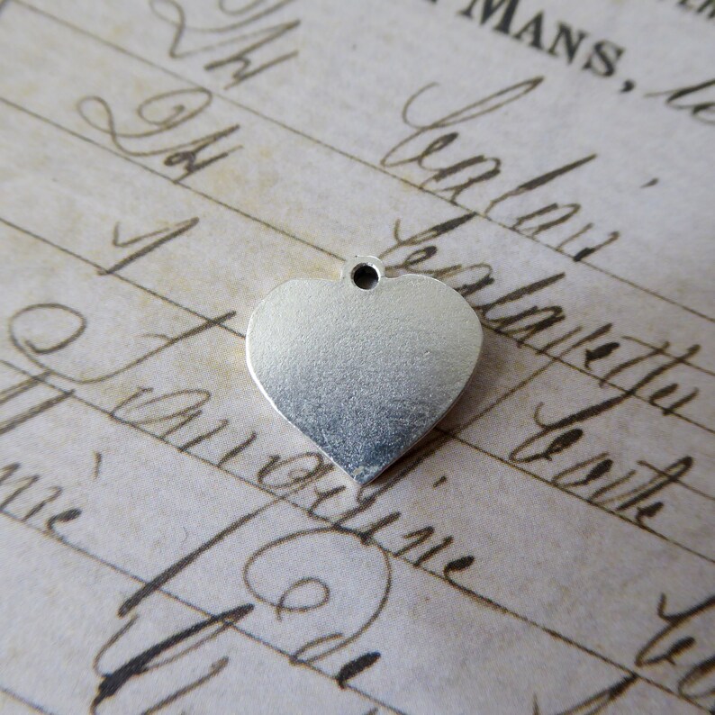 May include: A silver heart-shaped charm with a small hole at the top. The charm is smooth and shiny.