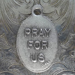 Pu&ograve; includere: Ciondolo ovale argentato con la scritta "PRAY FOR US". Il ciondolo ha un anello per appenderlo ed &egrave; contrassegnato "ITALY". Lo sfondo &egrave; una superficie argentata dettagliata e ornata con un motivo floreale.