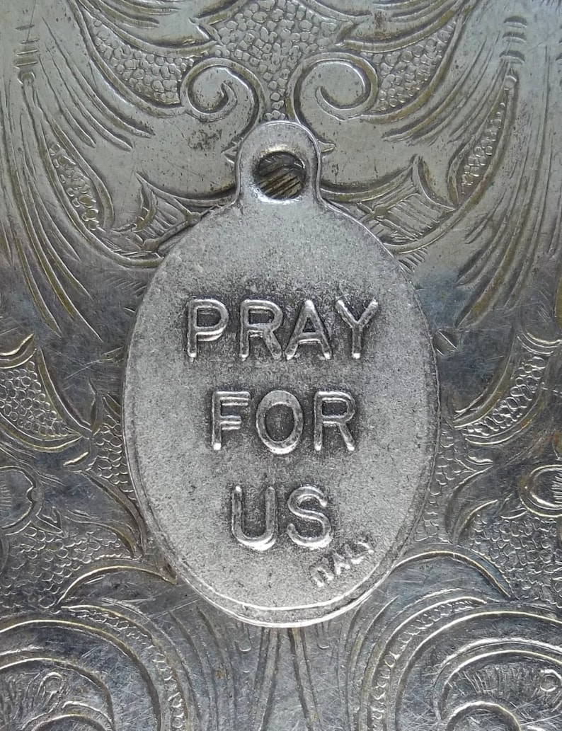 Pu&ograve; includere: Ciondolo ovale argentato con la scritta "PRAY FOR US". Il ciondolo ha un anello per appenderlo ed &egrave; contrassegnato "ITALY". Lo sfondo &egrave; una superficie argentata dettagliata e ornata con un motivo floreale.