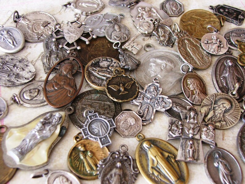 Peut inclure: Une collection de m&eacute;daillons, breloques et pendentifs religieux vintage en argent et en or. Les m&eacute;daillons pr&eacute;sentent divers personnages et symboles religieux, notamment la Vierge Marie, J&eacute;sus-Christ et des colombes.