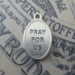 May include: Silver oval charm with the words "Pray for Us" and "Italy" inscribed on it.