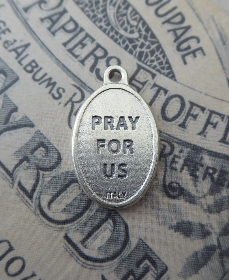 May include: Silver oval charm with the words "Pray for Us" and "Italy" inscribed on it.