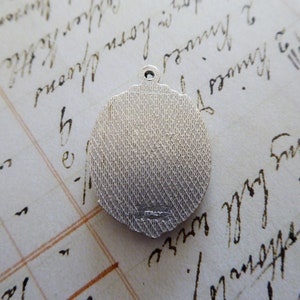 May include: Silver-toned round pendant with a textured surface and a small inscription on the back.