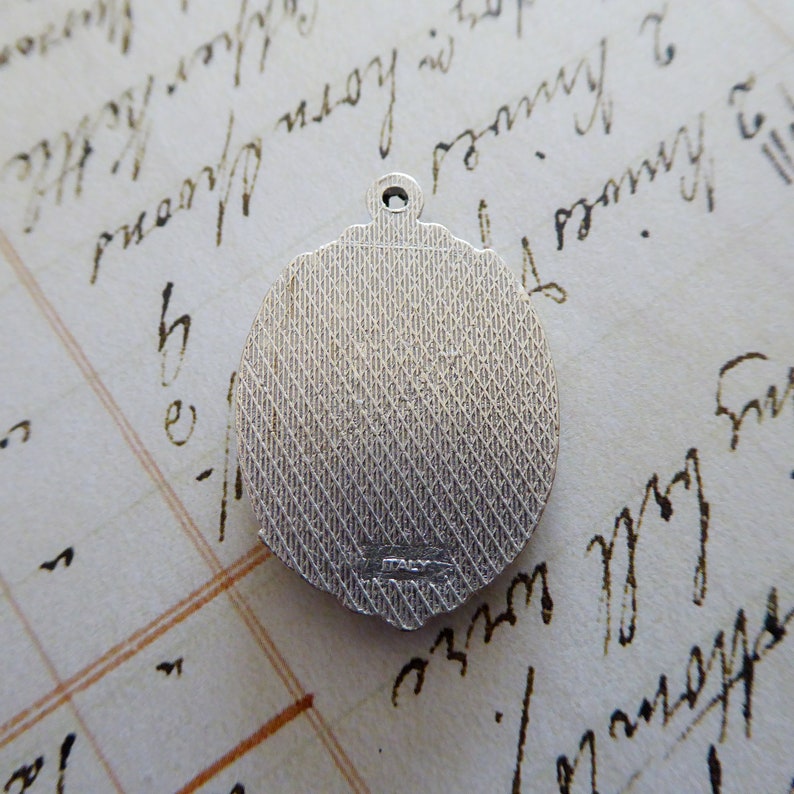 May include: Silver-toned round pendant with a textured surface and a small inscription on the back.