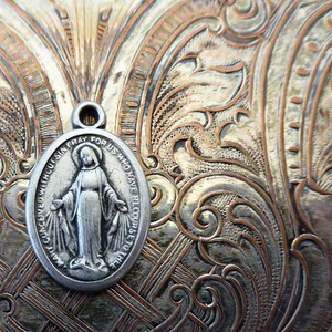 May include: Silver oval pendant with a depiction of the Virgin Mary and the text "CONCEIVED WITHOUT SIN, PRAY FOR US WHO HAVE RECOURSE TO THEE".
