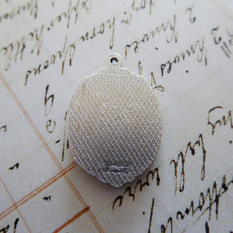 May include: Silver-toned round pendant with a textured surface and a small inscription on the back. The pendant has a loop at the top for attaching a chain.