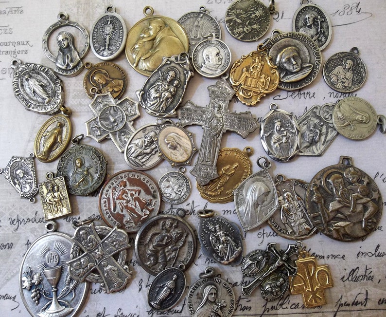 K&ouml;nnte beinhalten: Eine Sammlung antiker religi&ouml;ser Anh&auml;nger und Medaillen in verschiedenen Formen und Gr&ouml;&szlig;en. Die Anh&auml;nger bestehen aus silber- und goldfarbenen Metallen und zeigen detaillierte religi&ouml;se Figuren und Symbole. Einige haben aufwendige Kreuzdesigns, andere zeigen Heilige und biblische Szenen.
