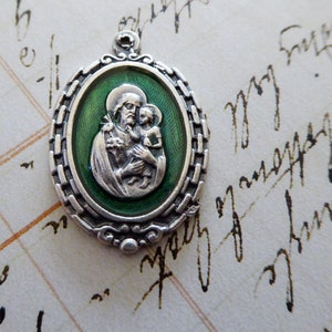 May include: Silver oval pendant with a green enamel background depicting Saint Anthony of Padua holding the Christ Child. The pendant has a detailed border.