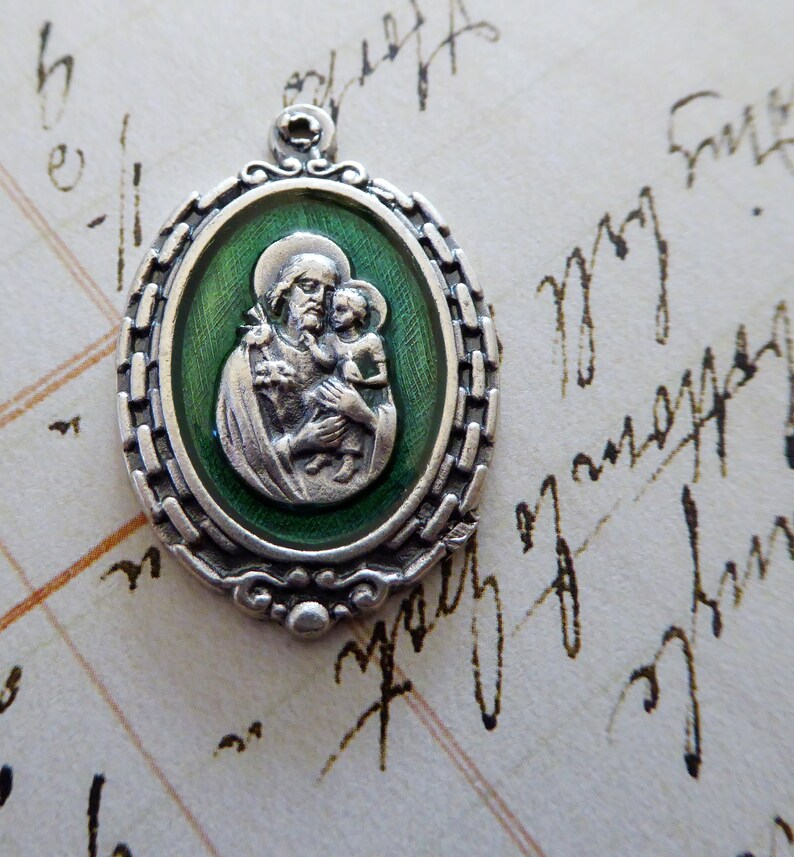 May include: Silver oval pendant with a green enamel background depicting Saint Anthony of Padua holding the Christ Child. The pendant has a detailed border.
