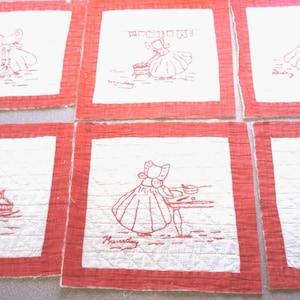 Peut inclure: Ensemble de six pièces de tissu carrées avec une bordure rouge et un centre blanc. Chaque pièce présente un dessin au trait rouge d'une figure à bonnet effectuant une tâche quotidienne, avec le jour de la semaine écrit en dessous. Le tissu a un aspect matelassé.