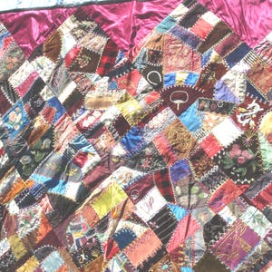 May include: A patchwork quilt with a rich array of colors and textures. The quilt features a diamond pattern composed of various fabric scraps, including floral prints, solid colors, and patterned textiles. The quilt is bordered with a deep burgundy fabric.