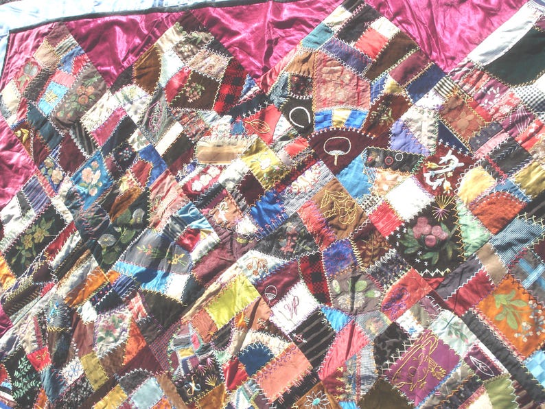 May include: A patchwork quilt with a rich array of colors and textures. The quilt features a diamond pattern composed of various fabric scraps, including floral prints, solid colors, and patterned textiles. The quilt is bordered with a deep burgundy fabric.