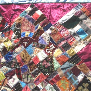 May include: A patchwork quilt with a rich array of colors and textures. The quilt features a variety of fabric squares in shades of red, brown, blue, and green, stitched together with white thread. The quilt's border is a deep burgundy color.