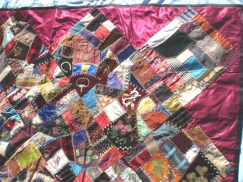 May include: A patchwork quilt with a rich array of colors and textures. The quilt features a variety of fabric squares in shades of red, brown, blue, and green, stitched together with white thread. The quilt's border is a deep burgundy color.