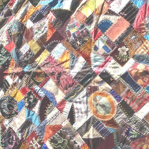 May include: A handmade quilt with a patchwork design. The quilt features a variety of fabrics in a mix of colors, including red, blue, green, and brown. Some patches have embroidered details. The quilt has a burgundy border.