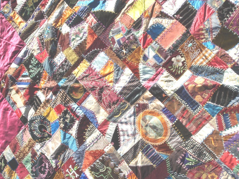 May include: A handmade quilt with a patchwork design. The quilt features a variety of fabrics in a mix of colors, including red, blue, green, and brown. Some patches have embroidered details. The quilt has a burgundy border.
