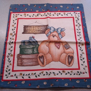 May include: A square fabric panel with a teddy bear illustration. The bear has a blue bow and a heart-shaped patch. The panel has a blue border with floral and insect designs, and a red and white inner border. The text "Antique Bears" is visible.