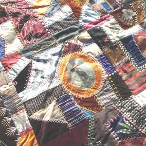 May include: Close-up of a handmade patchwork quilt with a variety of fabrics in shades of burgundy, brown, blue, and gold. The quilt features intricate stitching and a circular design in the center. A unique, handcrafted textile.