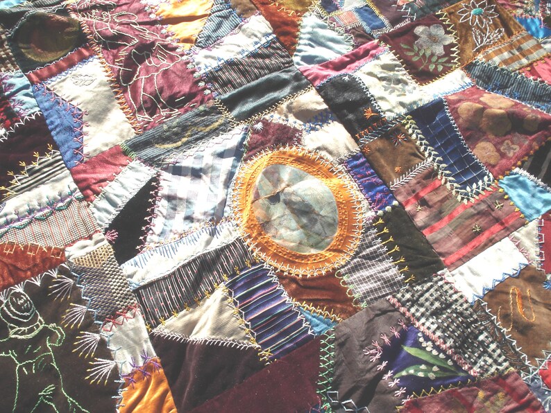 May include: Close-up of a handmade patchwork quilt with a variety of fabrics in shades of burgundy, brown, blue, and gold. The quilt features intricate stitching and a circular design in the center. A unique, handcrafted textile.