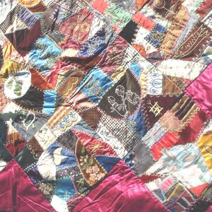 May include: A handmade quilt with a patchwork design. The quilt features a variety of fabrics in shades of brown, red, blue, and gold, with embroidered details. The border is a solid burgundy fabric.