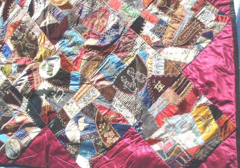 May include: A handmade quilt with a patchwork design. The quilt features a variety of fabrics in shades of brown, red, blue, and gold, with embroidered details. The border is a solid burgundy fabric.