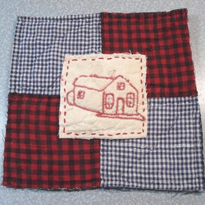 May include: A patchwork square with red and black buffalo check and blue and white gingham patterns. A smaller square in the center features a red embroidered house design on a cream-colored background.