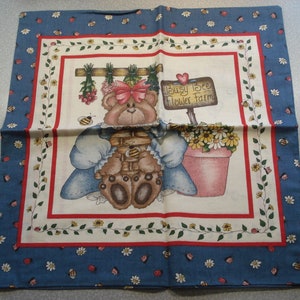 May include: A decorative fabric square featuring a cartoon bear holding a basket of honey, with the text "Busy Bee Flower Farm." The design includes a blue border with floral and insect motifs, and a central image of a bear and flowers.