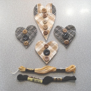 May include: Handmade fabric heart ornaments in various sizes and patterns, adorned with buttons. Two spools of embroidery floss, one tan and one black, are also present. These items are ideal for crafting and DIY projects.
