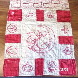 May include: A vintage, handmade quilt with a patchwork design. The quilt features red and white squares, with embroidered images of a dog, a cowboy on a crescent moon, and other motifs. The date "2021/09/30" is visible.