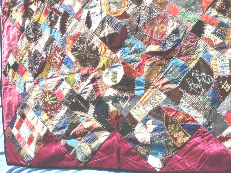May include: A colorful patchwork quilt with a deep red border. The quilt features a variety of fabrics in shades of blue, red, brown, and green, with embroidered details and geometric patterns. The quilt's dimensions are not visible.