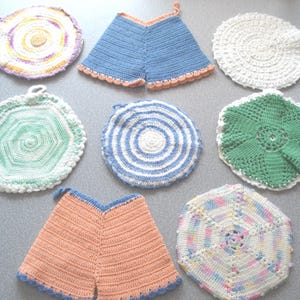 May include: A collection of handmade crochet pot holders in various shapes and colors. The pot holders include round, hexagonal, and triangular designs, with colors like blue, green, white, and peach. Some have scalloped edges.