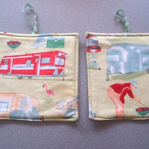 May include: Two square pot holders with a light yellow background. One features a red and white camper, the other a blue camper. Both have green hanging loops and camping-themed illustrations.