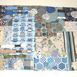 May include: A patchwork of blue fabrics, buttons, and embroidery floss. The design includes teacups, floral patterns, and geometric shapes. Various shades of blue and beige are used throughout the design. Buttons are in various sizes and shapes.