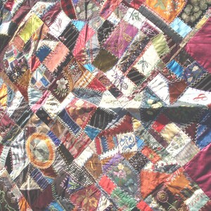 May include: A patchwork quilt with a variety of fabric patterns and colors. The quilt features a mix of geometric shapes and floral designs, with a deep burgundy border. The fabrics include velvet, silk, and other textiles.