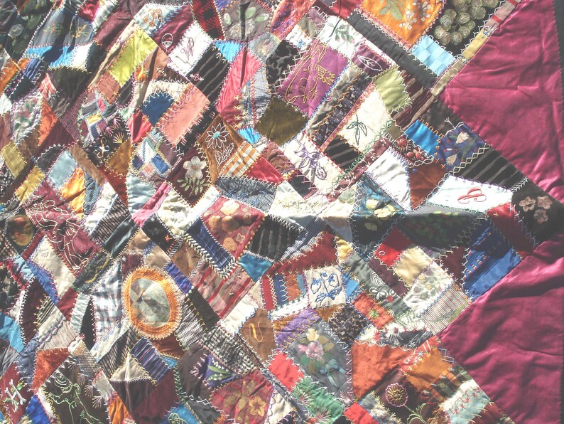 May include: A patchwork quilt with a variety of fabric patterns and colors. The quilt features a mix of geometric shapes and floral designs, with a deep burgundy border. The fabrics include velvet, silk, and other textiles.