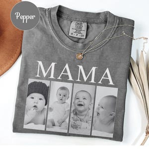 May include: A pepper-colored short-sleeve t-shirt featuring the word MAMA in white capital letters above a horizontal collage of four black and white photographs of infants. The shirt has a crew neckline and a Comfort Colors brand label inside.