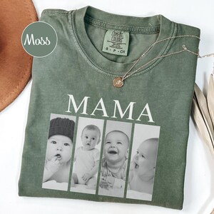 May include: A moss green short-sleeve t-shirt featuring the word MAMA in white capital letters above four vertical black and white photographic panels showing a baby in different poses. The shirt has a crew neckline and a Comfort Colors brand label.