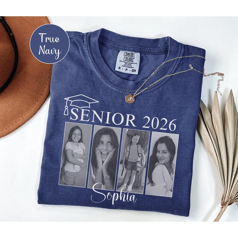 Puede incluir: Una camiseta azul marino con el texto "SENIOR 2026" y un gr&aacute;fico de gorro de graduaci&oacute;n. La camiseta presenta cuatro fotos en blanco y negro y el nombre "Sophia". Un collar dorado est&aacute; drapeado sobre la camiseta.