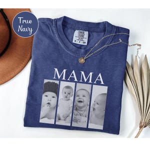 May include: A true navy blue short-sleeve t-shirt featuring the word MAMA in white capital letters above a horizontal collage of four black and white photographs of a baby. The shirt has a crew neckline and a Comfort Colors brand label.