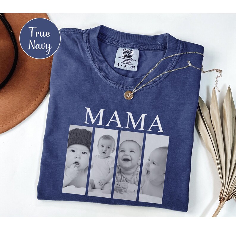 May include: A true navy blue short-sleeve t-shirt featuring the word MAMA in white capital letters above a horizontal collage of four black and white photographs of a baby. The shirt has a crew neckline and a Comfort Colors brand label.